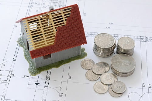 Das Bild zeigt ein Haus Neubau mit Geld und einem Bauplan